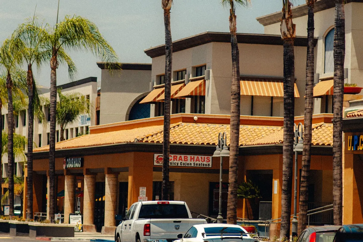 Shopping plaza with tile roofs, awnings and palm trees, with cars parked in front