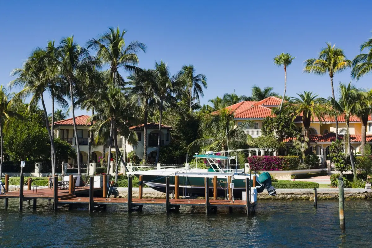 Wooden docks with a moored boat along a waterway, with tile-roofed homes and palm trees behind