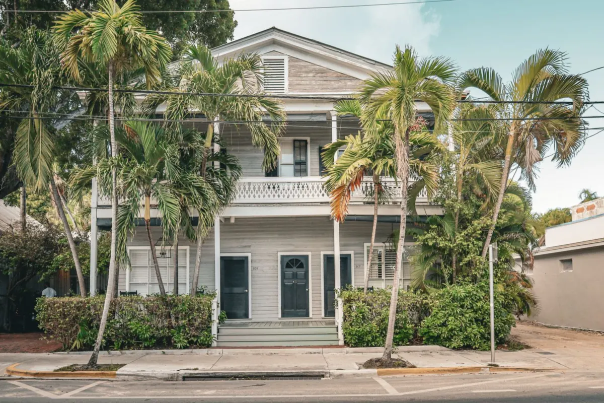 Two-story light gray clapboard house with a balcony and palm trees in front