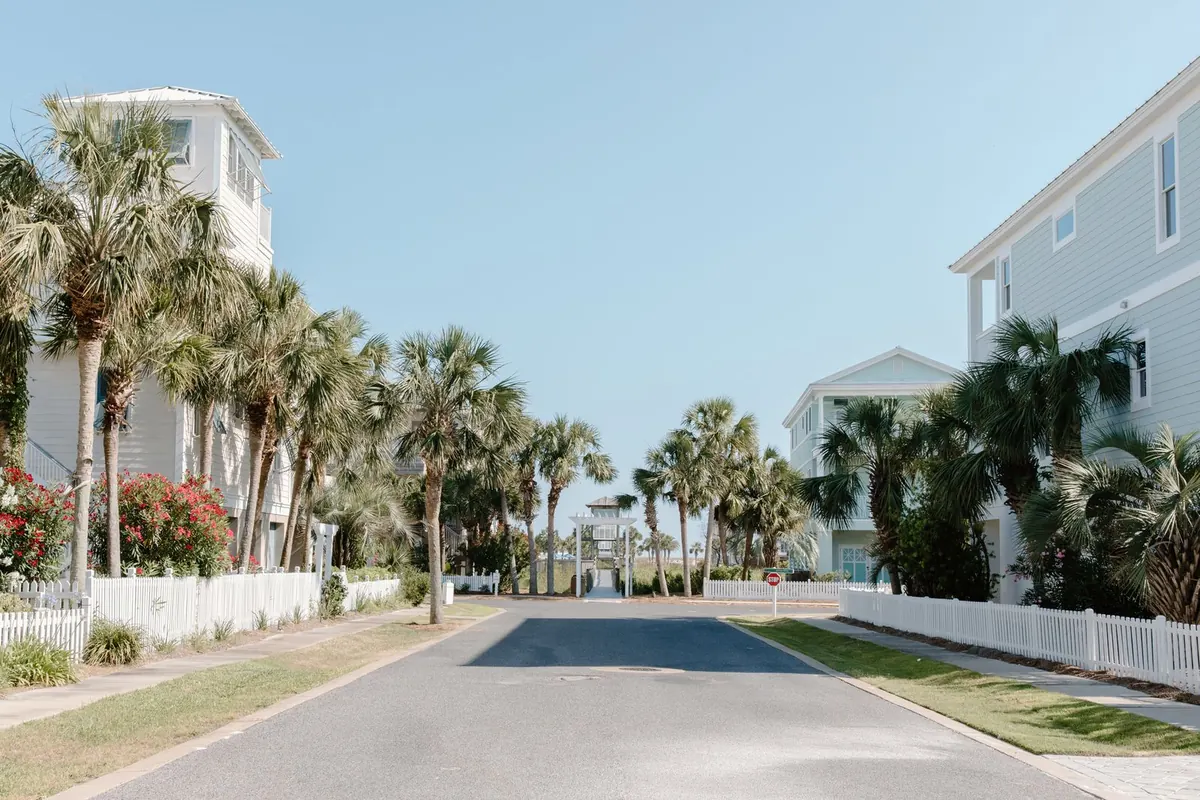 Quiet residential street lined with palm trees, white fences and light-colored houses