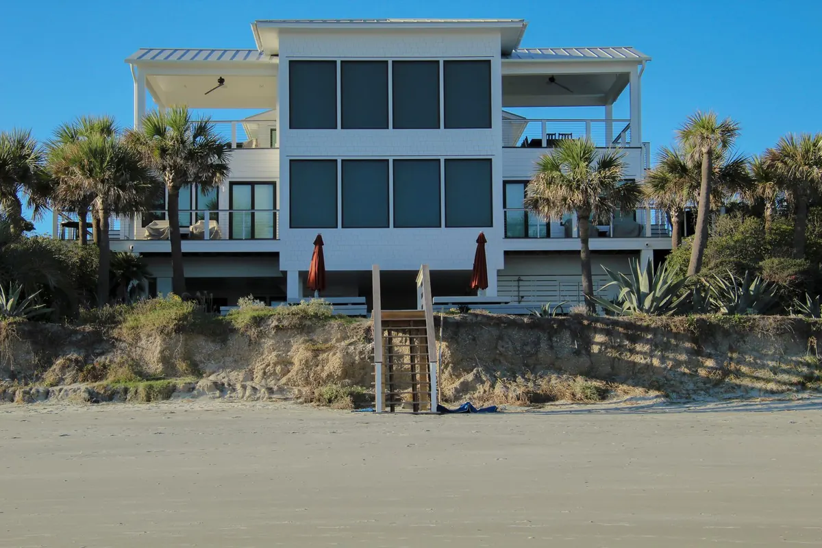 Modern raised beachfront house with palm trees and a wooden stair down to the sand