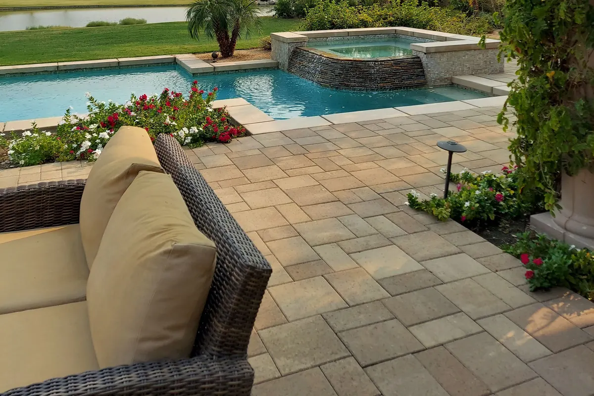 Clean, sealed beige pavers on a pool deck beside a spa and flower beds