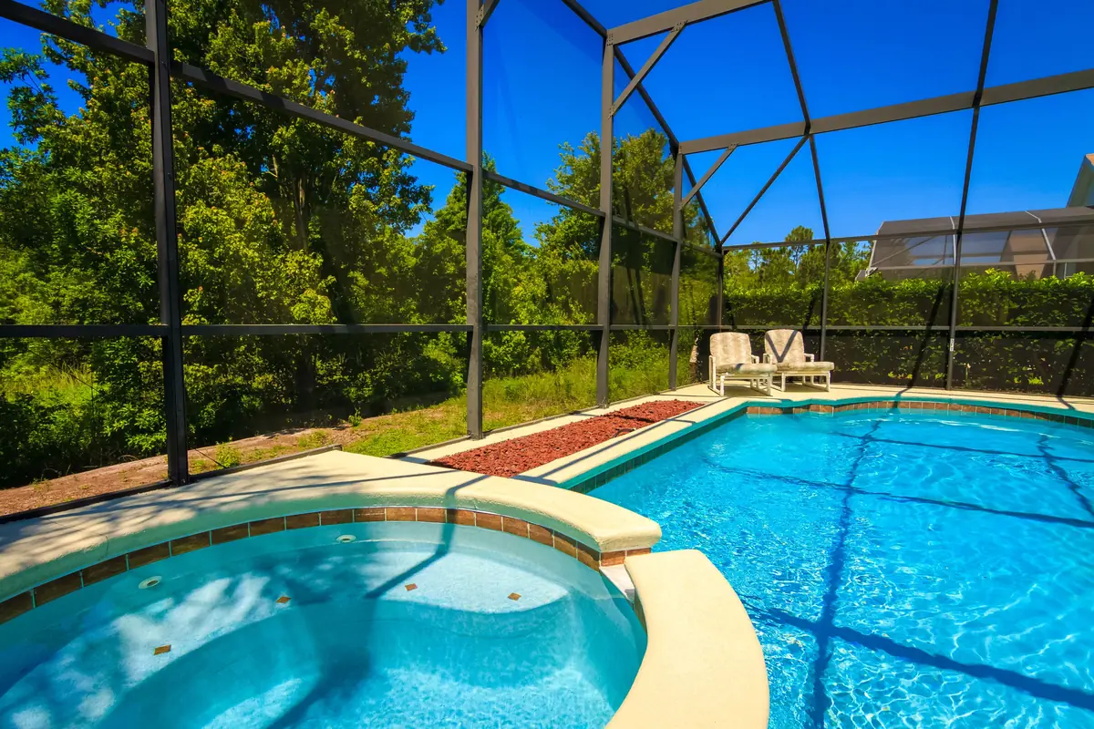 Screened aluminum pool cage over a pool and spa, with trees beyond the screen